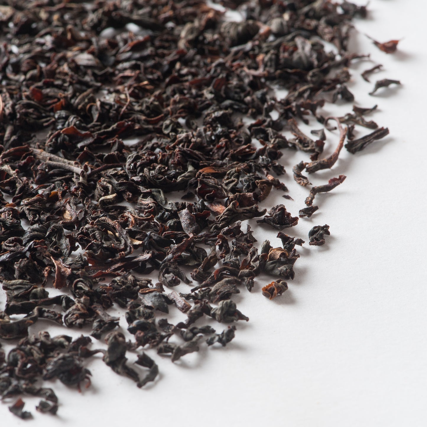 Loose dark tea leaves with curled edges scattered on a white surface.