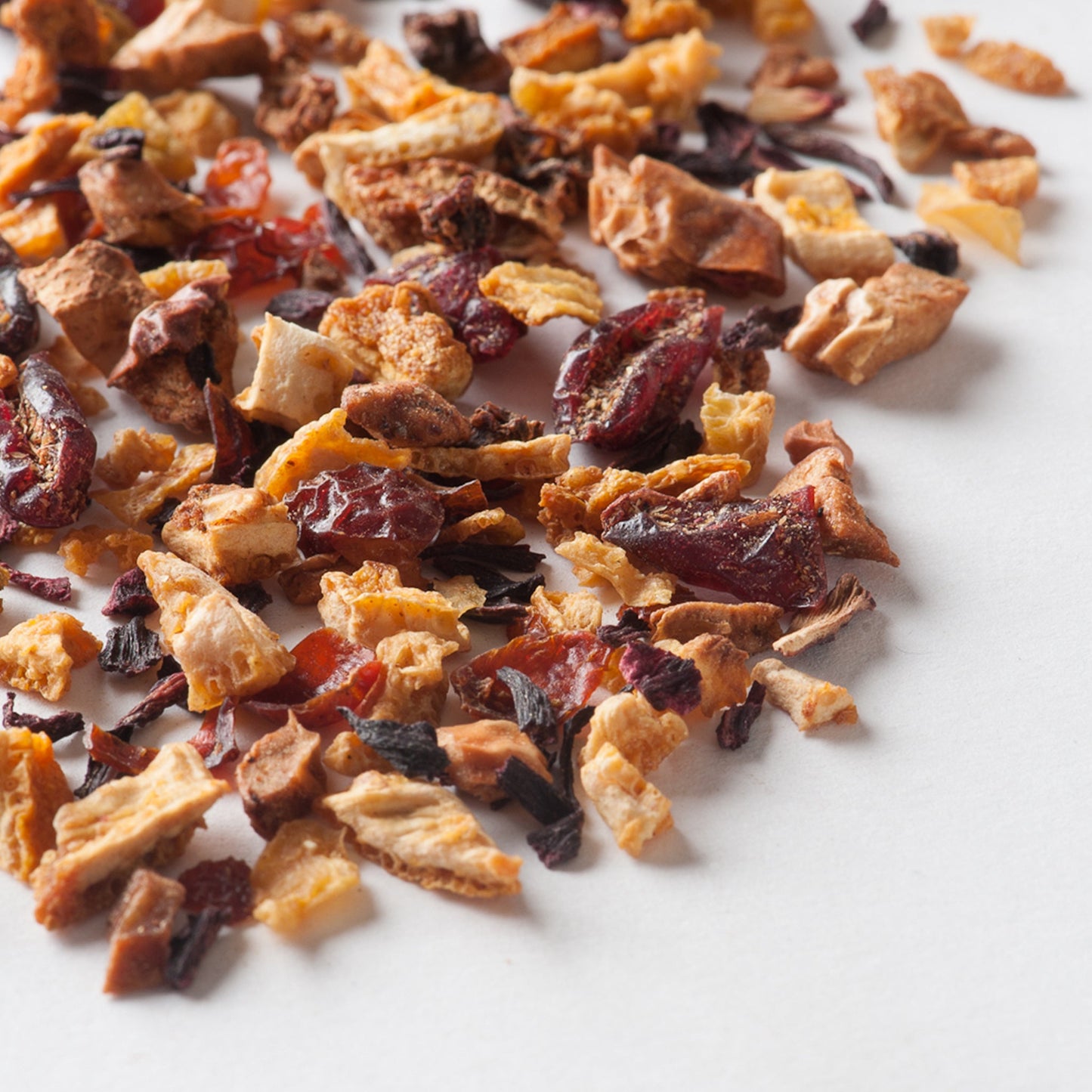 Dried tea blend with orange peel, blood orange pieces, and dark herbs scattered on white surface.