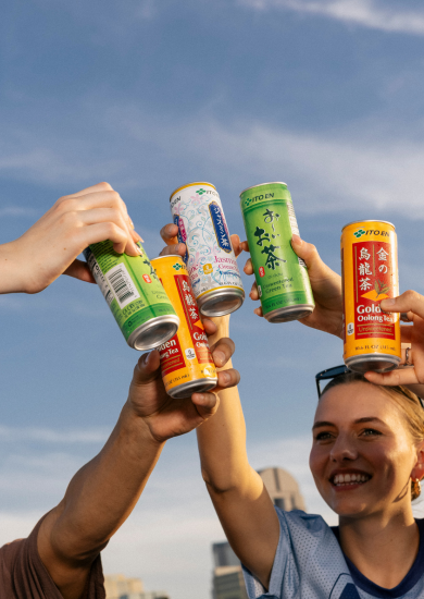 Hands cheering with cans of Ito Ens Oolong tea, Jasmine green tea, and Oi Ocha green tea