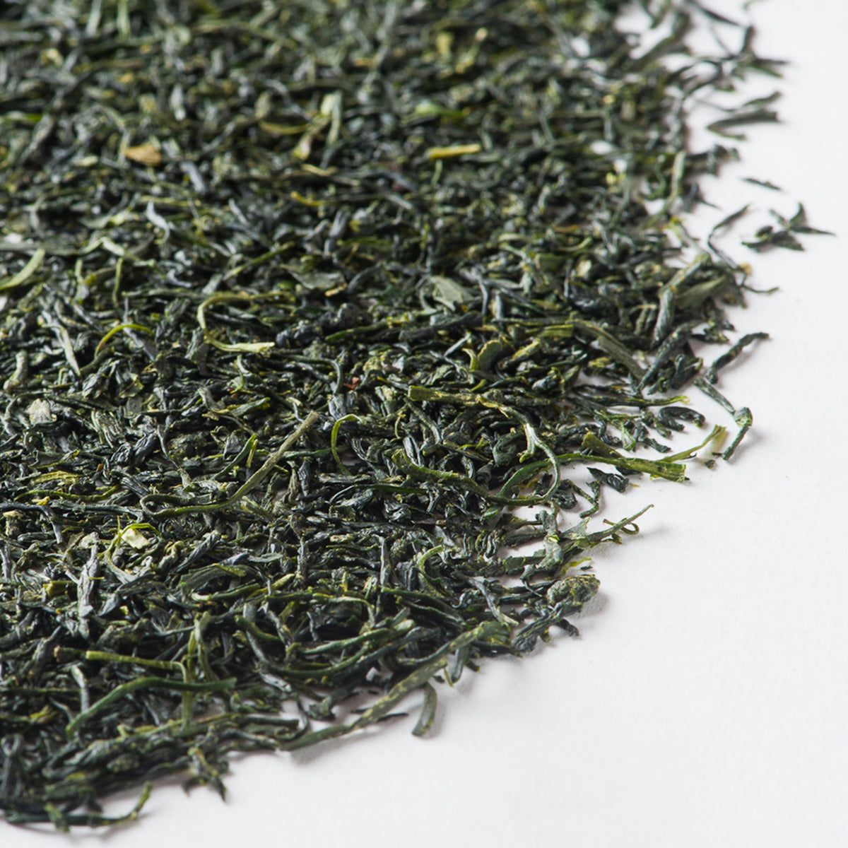 Loose green tea leaves with thin, needle-like strands in dark green and yellow tones on white background.